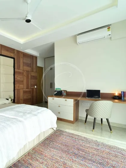 This view of the bedroom showcases the long, integrated study desk, providing a spacious and functional workspace. The design maintains the room's minimalist aesthetic with clean lines and a simple color palette.