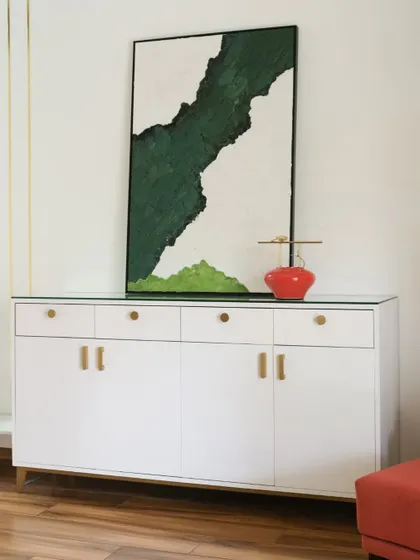 A minimalist white sideboard provides clean and simple storage. It becomes a stylish focal point with the addition of a stunning abstract painting and a pop of color from a bright red vase.