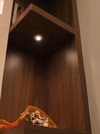 A close-up of a spotlight inside a dark wood shelf, highlighting a small idol in a puja unit.