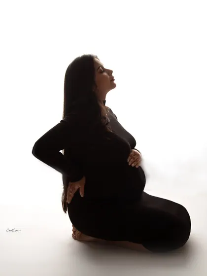 A powerful and artistic silhouette. This kneeling pose in a simple black dress creates a dramatic and timeless fine-art maternity portrait.
