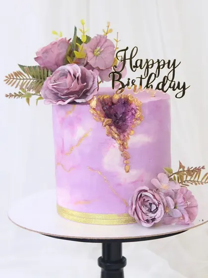 A gorgeous lavender geode cake perfect for a princess. This design has a marble-like finish, a sparkling amethyst-inspired sugar geode, and is adorned with matching purple flowers.