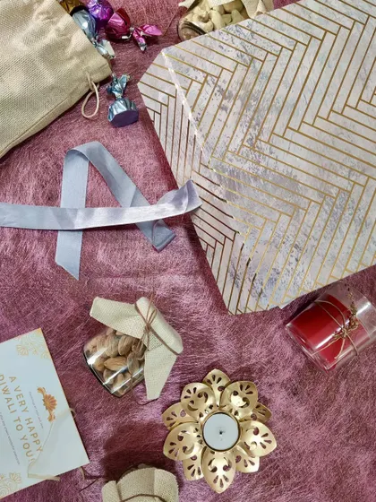 A collection of items ready to be packed into a Diwali hamper. We bring together gourmet snacks, a scented candle, and a decorative diya holder for a complete festive experience.