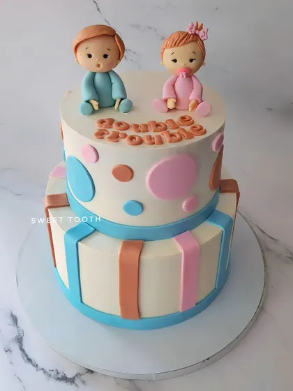 Double trouble! A two-tier chocolate truffle cake for a twin's birthday, decorated with cute baby figurines and a gift box theme.