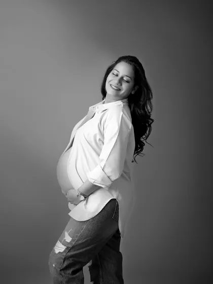 A joyful black and white portrait of a mom-to-be. Her happy smile and the casual styling with an open shirt and jeans create a feeling of relaxed and glowing motherhood.