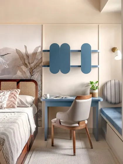 The study nook is perfectly integrated beside the bed, featuring a minimalist blue desk and a uniquely shaped wall shelf. This compact corner is designed for focus without disrupting the room's restful mood.