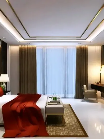 A bedroom design that exudes luxury, with a striking red bedspread, a false ceiling with gold trim, and a dedicated dressing table area.