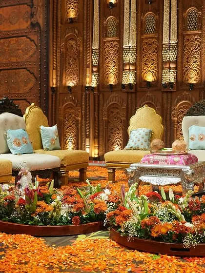 The seating area for the South Indian wedding featured custom furniture and a floor covered in orange flower petals. The backdrop of intricately carved wooden panels continued the theme of regal elegance.