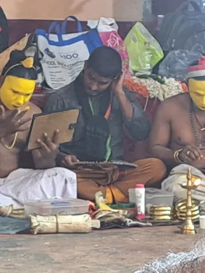Artists applying the distinct yellow face paint for the Dhumavati kola, using a small mirror.