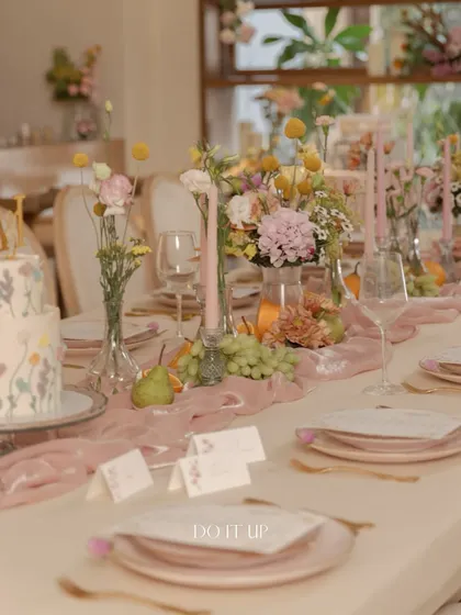 An elegant tablescape for an anniversary brunch. The table features dusty pink plates, a soft velvet runner, and delicate centerpieces of wildflowers, creating a romantic and sophisticated setting.