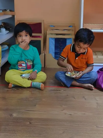 Children sitting in a line, patiently enjoying the snacks they made. This simple moment teaches important social skills like waiting for one's turn and enjoying a meal as a community.