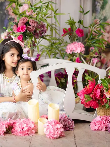Two sisters posing together on a white bridge amidst a garden of flowers. This portrait highlights their sweet and loving relationship.