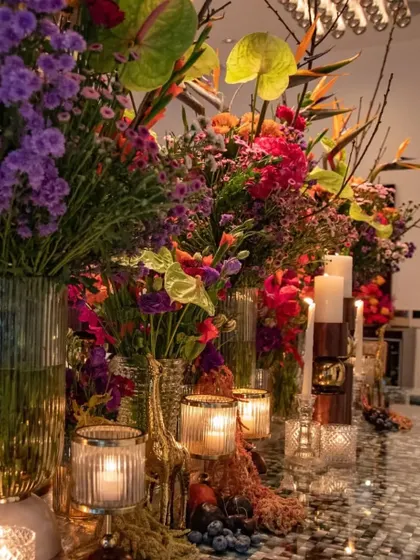 A view of the tablescape showing the layers of glass vases, candles, and colorful flowers. The design creates a sense of depth and abundance, inviting guests to look closer.
