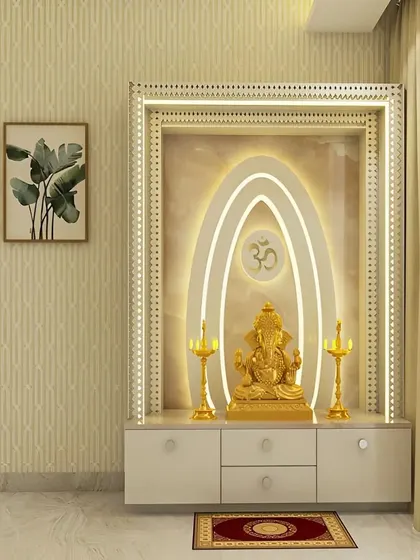 This elegant pooja unit features a distinctive backlit design with concentric ovals framing a central OM symbol. The off-white cabinet with a marble-like countertop provides a sophisticated and modern platform for the main idol and brass lamps.