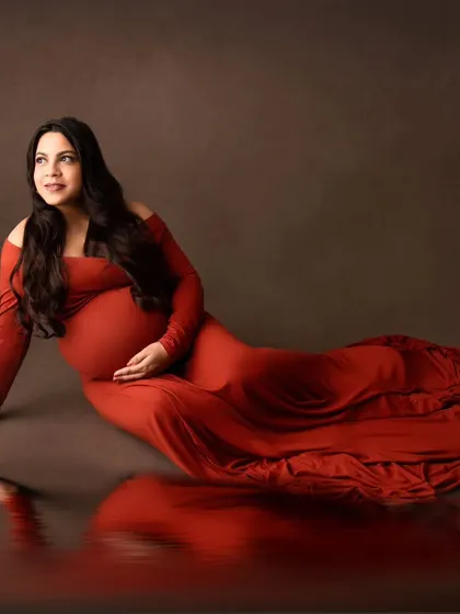 An artistic portrait with a beautiful reflection effect. The mom-to-be is lying gracefully in a burnt-orange gown.
