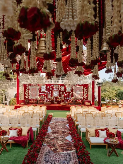 A view of the 'Laal Ishq' wedding ceremony setup from the guest's perspective. The combination of hanging floral strings, a rich red backdrop, and traditional seating created an immersive and culturally rich experience.
