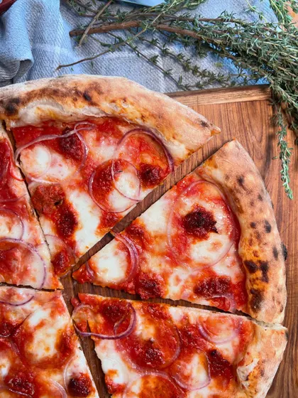 Our Goan Sausage pizza, beautifully arranged on a wooden board with fresh thyme.