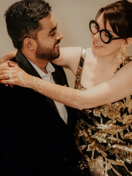 An intimate, warm-toned photo of the couple sharing a close moment. The bride's henna-adorned hands add a traditional touch to this modern, romantic portrait.