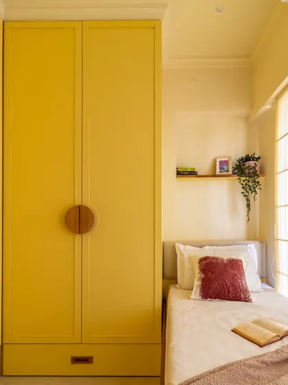 The full-height yellow wardrobe with unique wooden handles maximizes vertical storage while adding a bold design statement to this compact room.