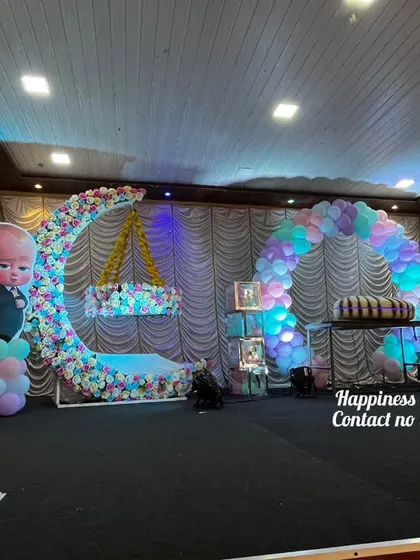 A Cocomelon-themed naming ceremony, combining a popular cartoon with traditional elements. The stage includes a floral moon-gate with a cradle, a balloon arch, and character cutouts.