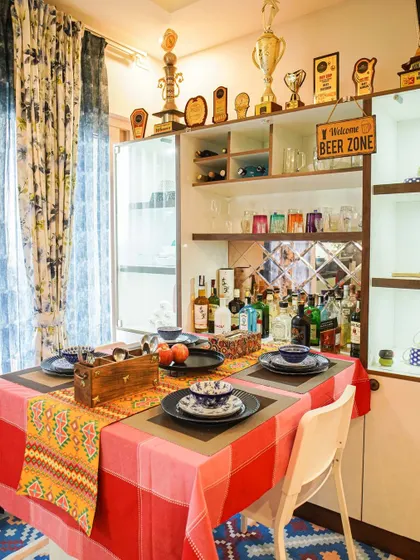 A vibrant dining area featuring a custom bar and crockery unit. The space is personalized with trophies and a "Welcome Beer Zone" sign, reflecting the client's personality.
