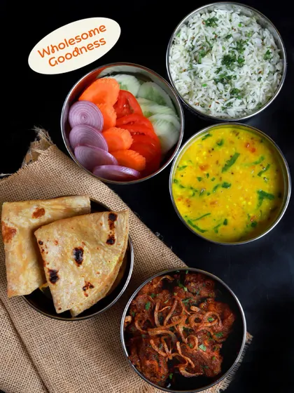 A simple yet hearty meal against a dark backdrop. This tiffin includes a flavourful meat curry, dal, soft rotis, and a fresh salad, showcasing a complete and balanced non-veg option.