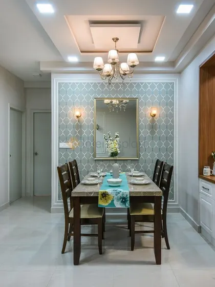 An elegant dining room featuring a classic chandelier, patterned wallpaper, and a mirror to create a sense of space. The false ceiling design adds a layer of architectural detail.