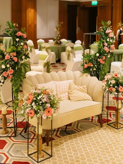 A comfortable and stylish seating area created for a milestone birthday party. We paired a classic scalloped sofa with modern floral stands filled with pink and white roses to create a perfect spot for photos.