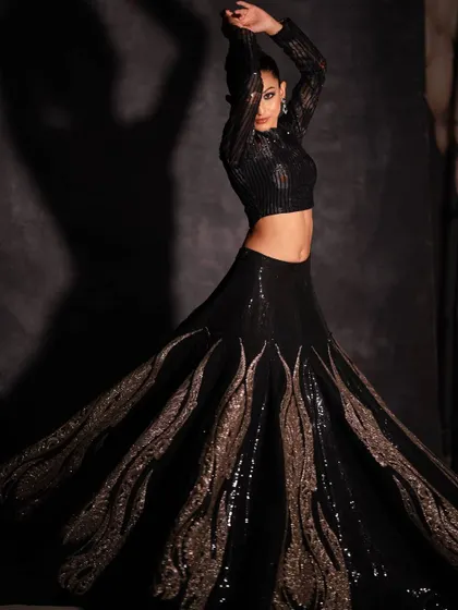 This fusion lehenga is for the bold and modern woman. The structured, shimmering black skirt with its unique wave-like embellishments creates a dramatic, avant-garde silhouette, paired with a sleek sequined crop top.