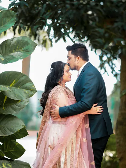 An intimate moment during an outdoor reception, with the groom kissing the bride's forehead.