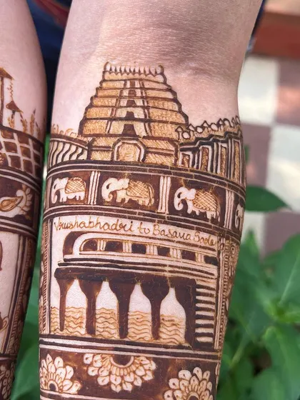 A detailed shot of the temple and meeting spot motifs. The design captures the exact location where the couple's journey began, making it a cherished part of their mehendi.