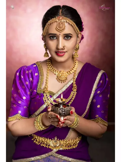 A client looking divine in a traditional purple saree with a puff-sleeve blouse, holding a diya for a festive photoshoot.