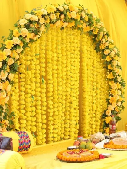 A sunny yellow Haldi setup with a floral arch made of marigolds and roses. The seating area is decorated with traditional printed cushions.