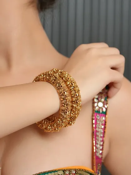 A shot centered on a pair of heavy, intricately carved gold bangles. This type of photo is essential for e-commerce, showing the product's design from a wearable perspective.