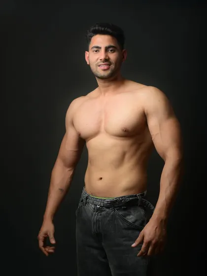 A classic physique shot against a clean, dark background. The lighting is carefully controlled to define muscle and showcase the results of hard work in the gym.