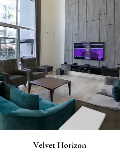 A vibrant living room in a duplex, where a teal velvet sofa and grey armchairs create a sophisticated color story against a textured, paneled TV wall.