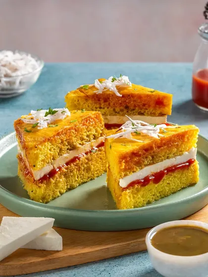 A creative Dhokla Sandwich, with layers of dhokla, chutney, and paneer, garnished with grated coconut.