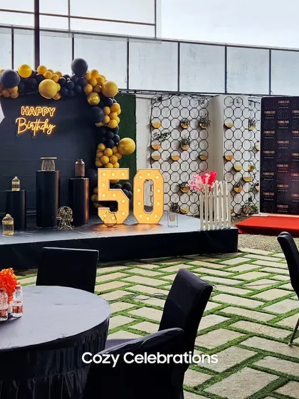A wide view of the 50th birthday party venue, showing the main photo backdrop, stage, and guest seating arrangements.