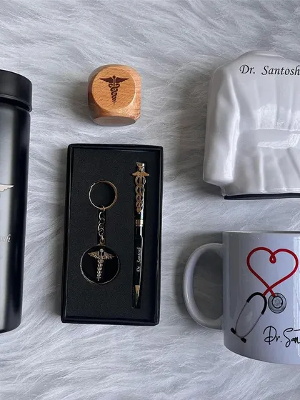 A specialized gift set for doctors, shown here with all items unboxed. The combo includes a personalized turbo bottle, a doctor coat pen stand, a ceramic mug, a pen and keychain set, and a wooden paperweight, all with a name and doctor logo.