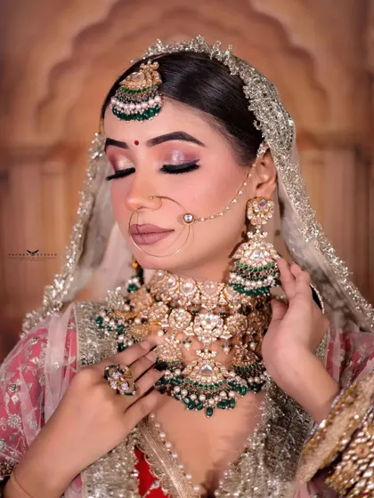 A stunning close-up portrait focusing on the bride's flawless makeup and heavy kundan and emerald jewellery. Her eyes are closed, giving the photo a serene and peaceful feel.