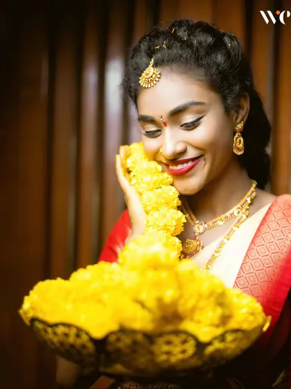 A joyful bride during a pre-wedding ritual. Her smile as she holds a bowl of yellow flowers is infectious, and we capture these moments of pure happiness.