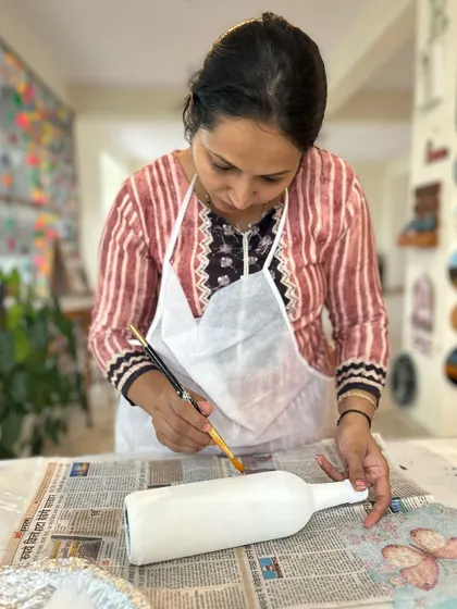 A participant carefully painting a base coat on a bottle before applying the decoupage paper.
