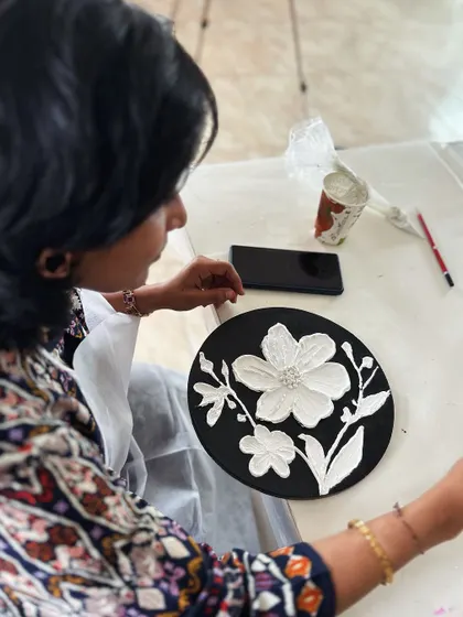 An artist adding the final touches to her textured floral artwork.
