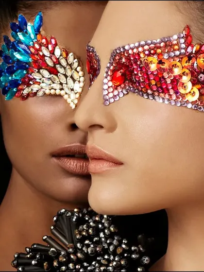 A conceptual beauty shot featuring two models with ornate, jeweled eye masks. This image is about texture, color, and symmetry, creating a visually rich and artistic statement.