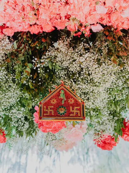 A detailed shot of a traditional toran, adorned with auspicious symbols. We hung this piece amidst a canopy of pink carnations and baby's breath, ensuring that even the smallest ritualistic elements are beautifully presented.