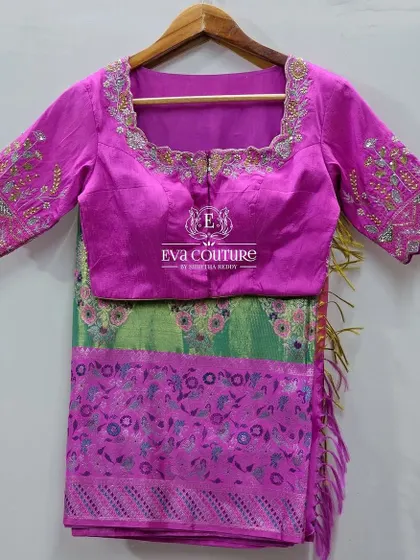 A beautiful saree blouse in magenta with intricate floral embroidery on the back and sleeves. This piece is designed to complement the green and pink saree.
