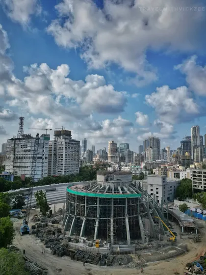 A drone's eye view of a circular building under construction in Dadar, surrounded by the dense urban fabric of the city, showcasing ongoing development.