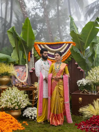 A beautifully coordinated couple on their wedding day, set against a stunning backdrop of traditional floral decor. This look captures the essence of a vibrant, modern Maharashtrian wedding, blending a classic yellow Paithani saree with a contemporary pink shela and a custom-designed groom's outfit.