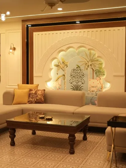 A heritage-inspired living room featuring a large L-shaped sofa and a traditional wooden coffee table. The focal point is the arched wall niche with intricate artwork, framed by dark wood, which adds a touch of Rajasthani royalty. The design balances modern comfort with timeless Indian aesthetics.