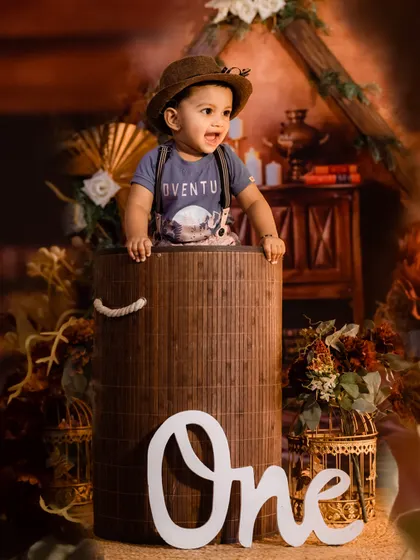 An adventurous theme for a first birthday, with the birthday boy peeking out of a large barrel in a rustic, explorer-style setup.
