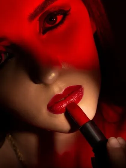 A dramatic, low-key beauty shot of a model applying red lipstick, with a red light gel creating a moody and intense feel. This style is perfect for bold makeup campaigns and editorial features.